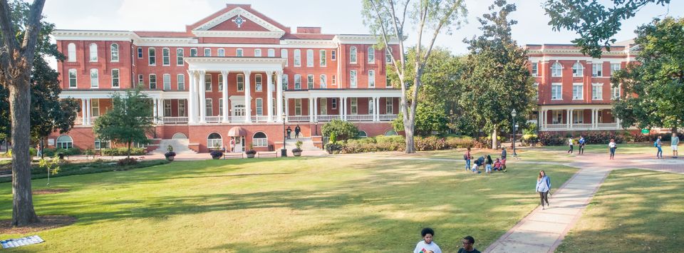 Summer camp activities at a college campus with students enjoying the green lawn and historic brick buildings.