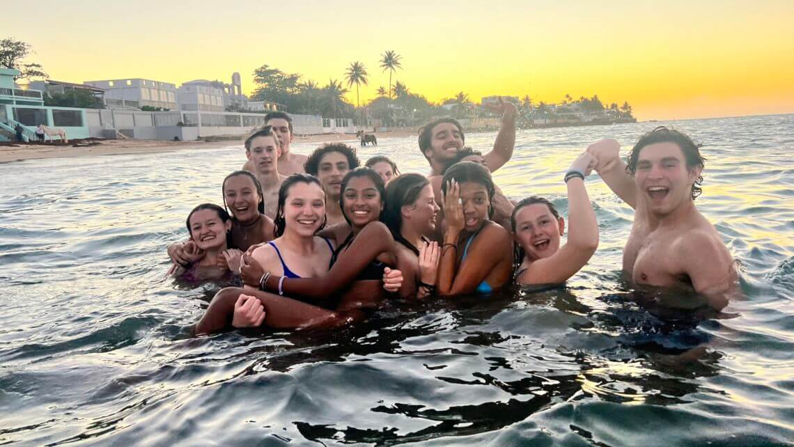 Group of teens enjoying a summer beach experience during a hurricane relief program in Puerto Rico at sunset.