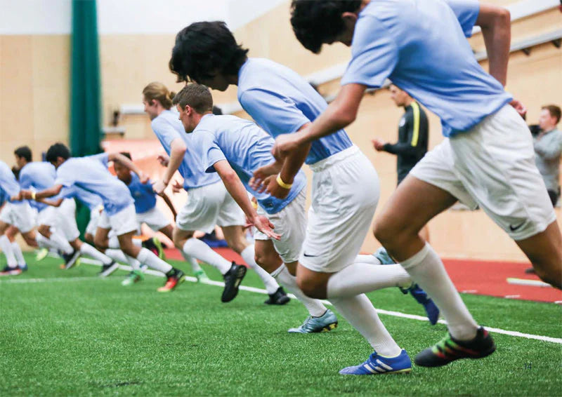 Boys in blue jerseys sprinting during a soccer training session on turf, emphasizing teamwork and athletic development.