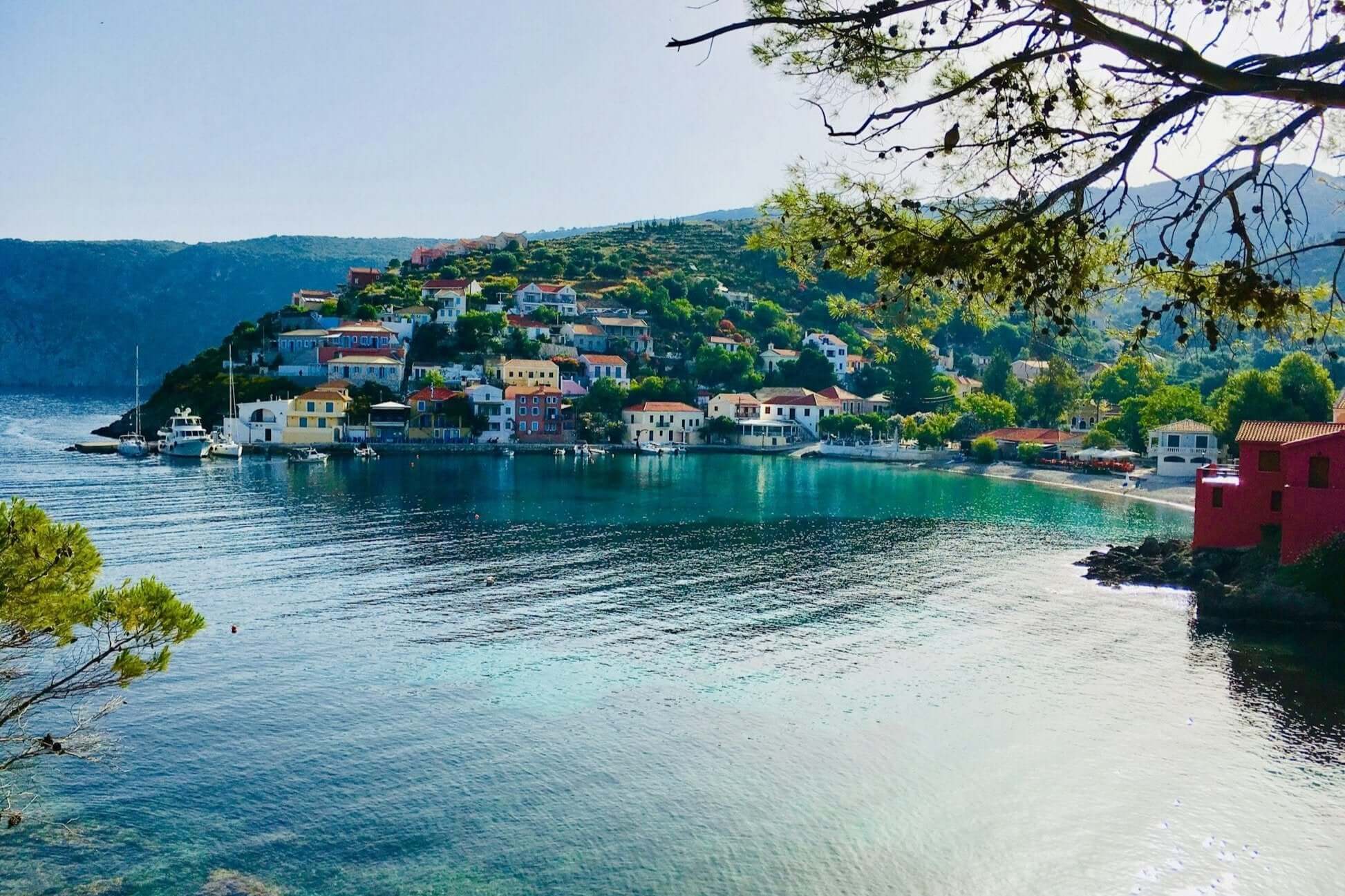 picturesque harbor view of a Greek Ionian Island, showcasing colorful houses along the shore and clear blue water.