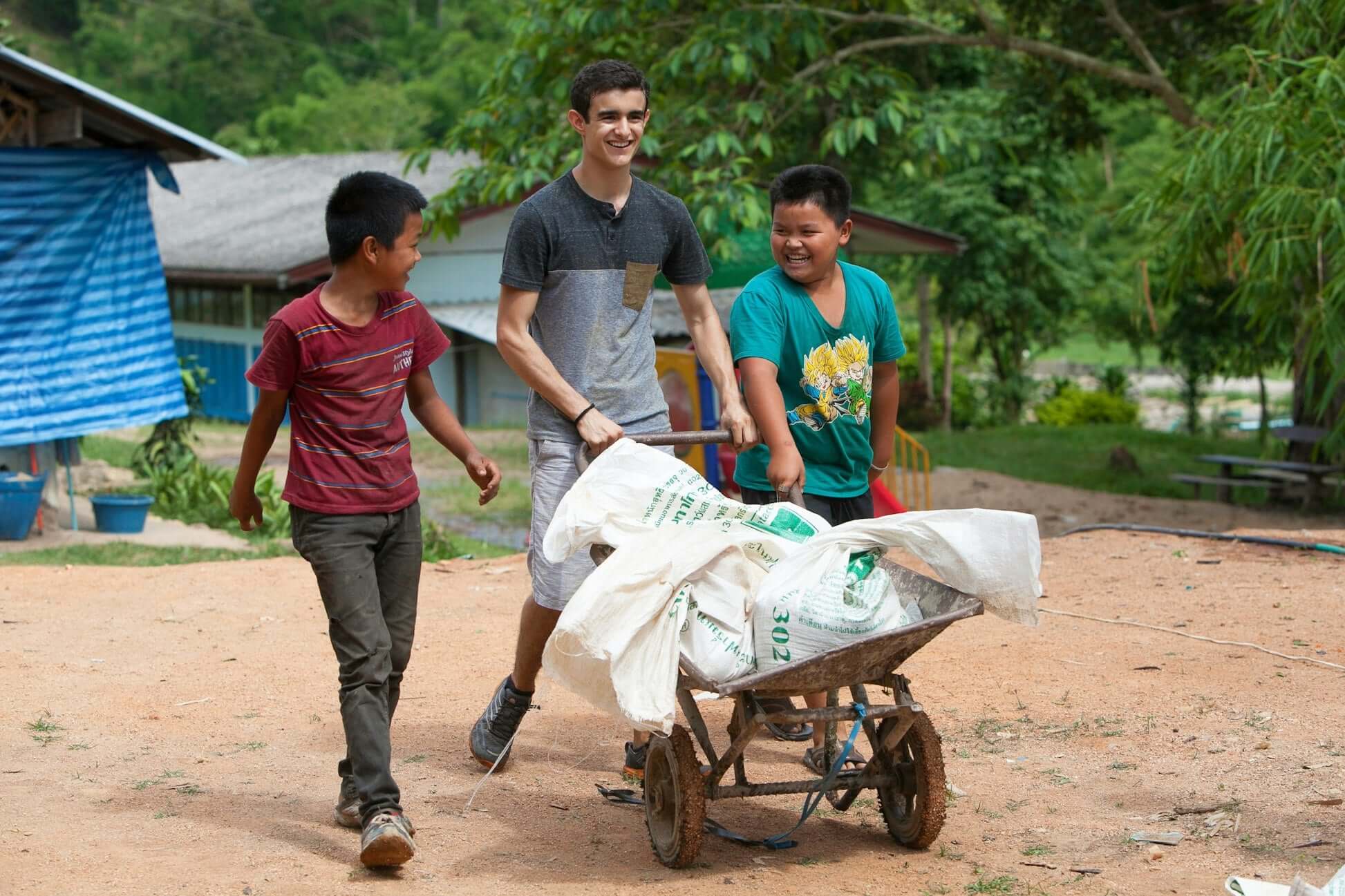 Teen volunteers helping in Thailand while carrying supplies in a wheelbarrow during a community service expedition.