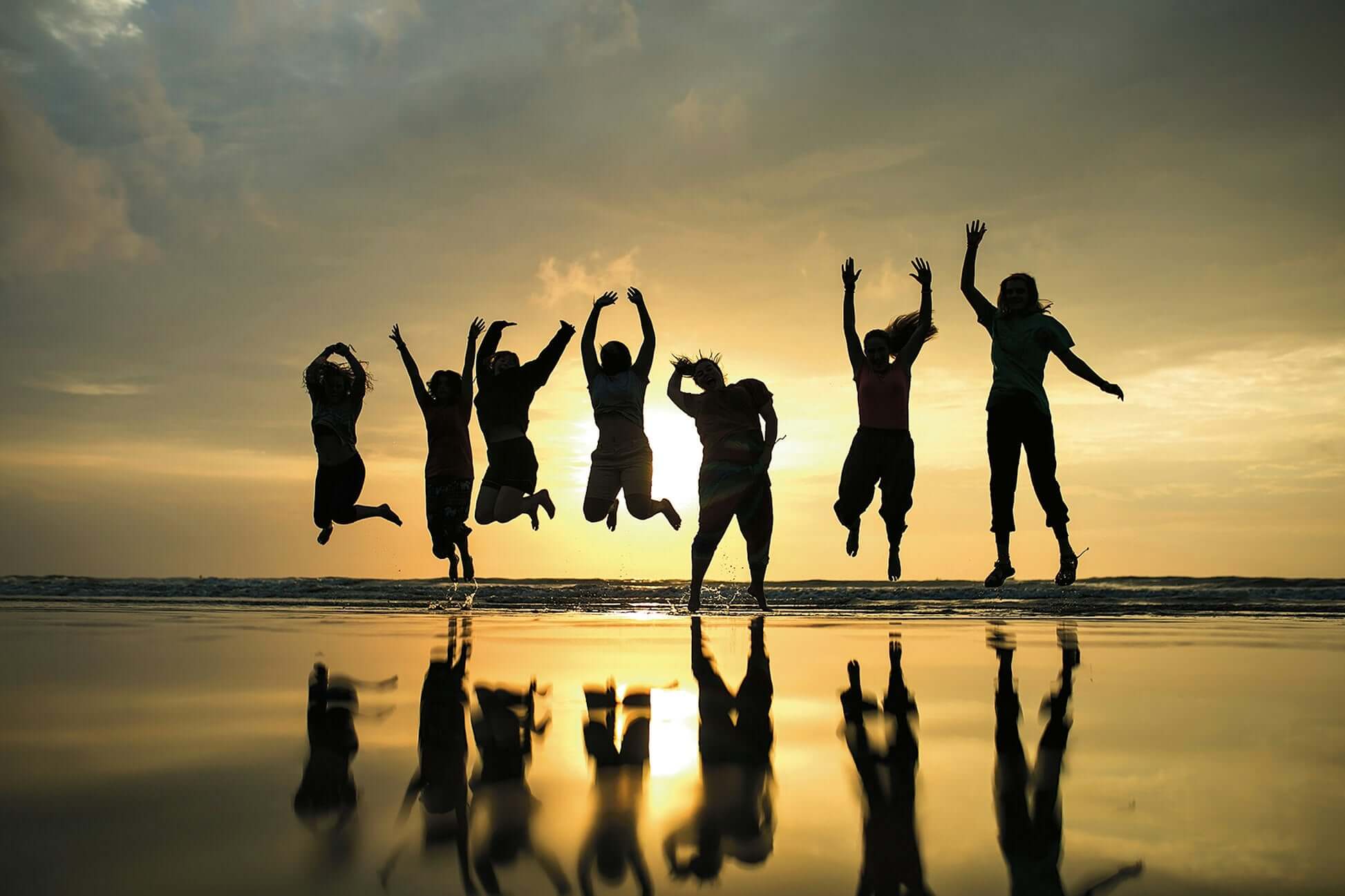 Group of happy travelers jumping on the beach at sunset, capturing the joy of student travel in Thailand.