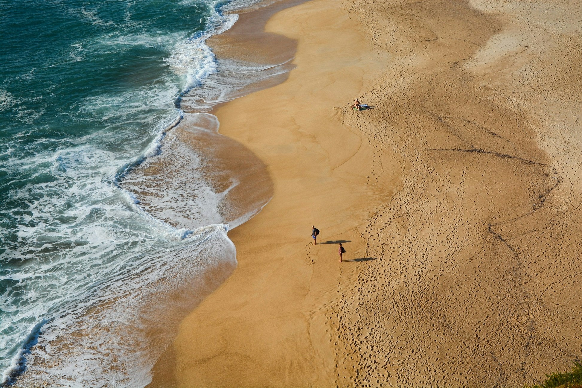 two people walking along a sandy beach near the ocean waves in Portugal, perfect for teen travel and summer programs.