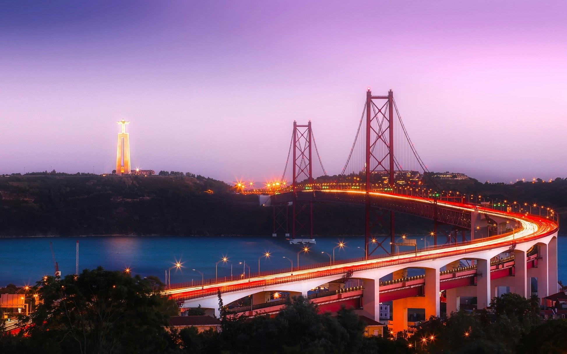 Stunning view of Lisbon's bridge illuminated at dusk, with the Cristo Rei statue in the background, capturing Portuguese beauty.