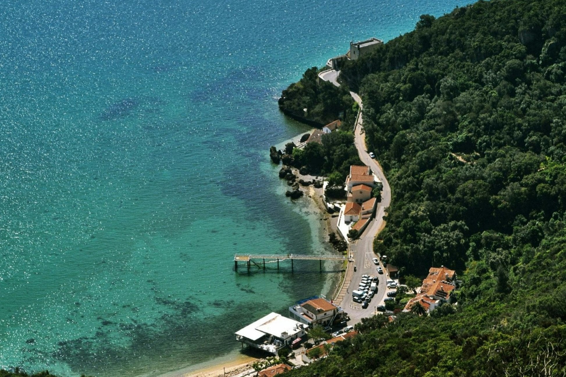Aerial view of a picturesque coastal village with clear turquoise water and lush greenery in Portugal.