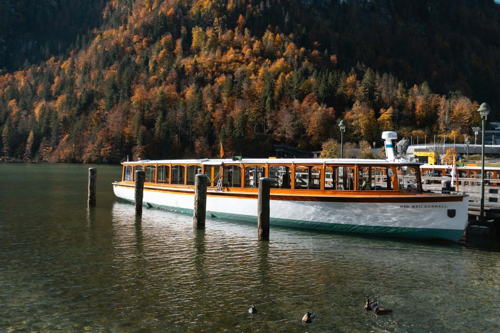 Scenic wooden boat docked at a pier surrounded by colorful autumn trees in Bavaria, Germany.
