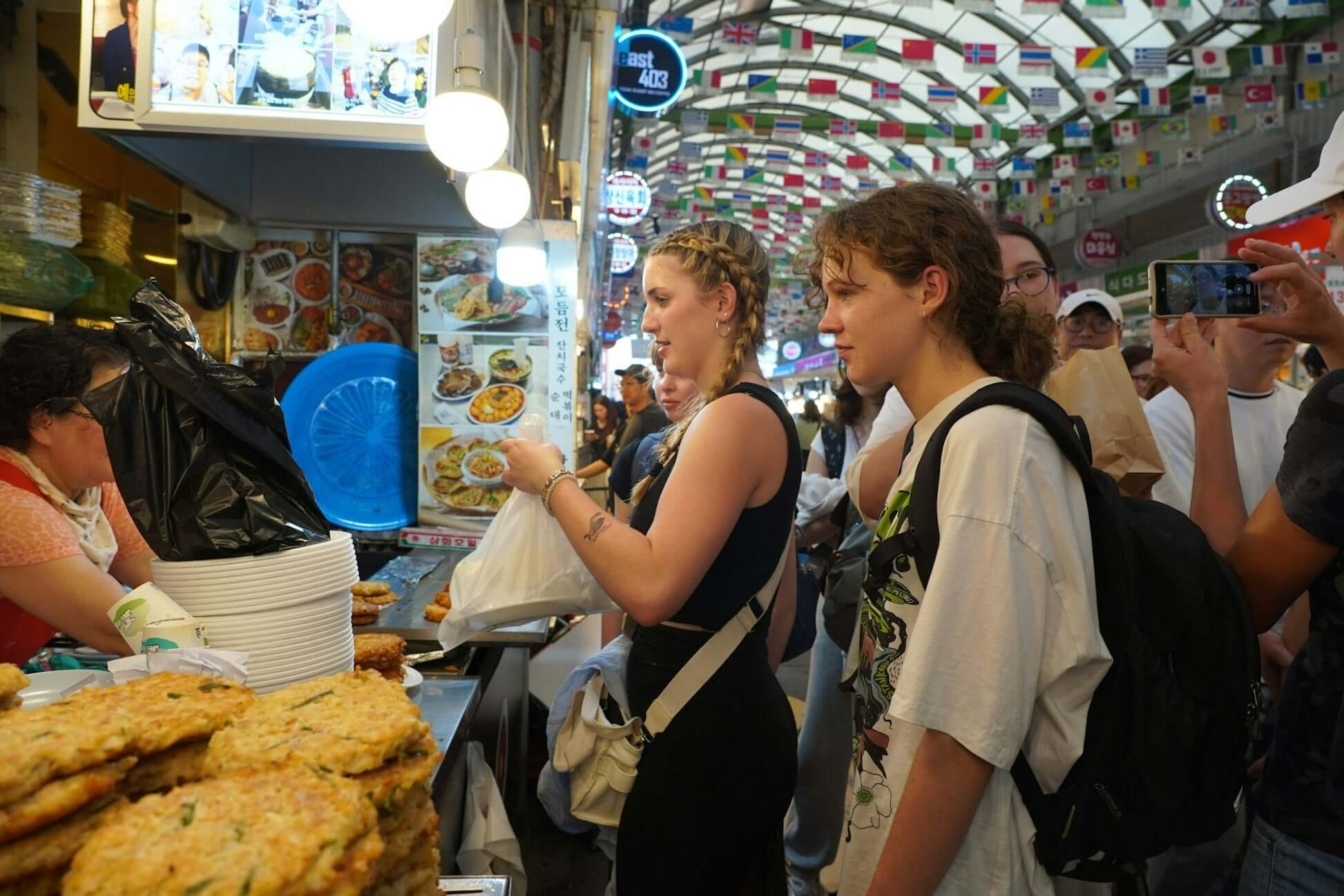 teens exploring a bustling South Korean market, enjoying local food and cultural experiences during their summer travel program