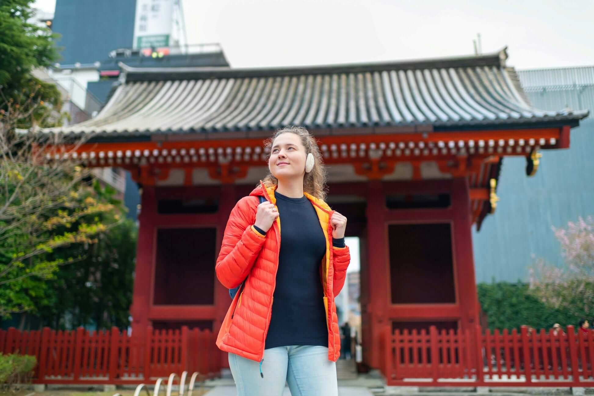 Young woman in a red jacket enjoying her visit at a traditional Asian temple with vibrant architecture.