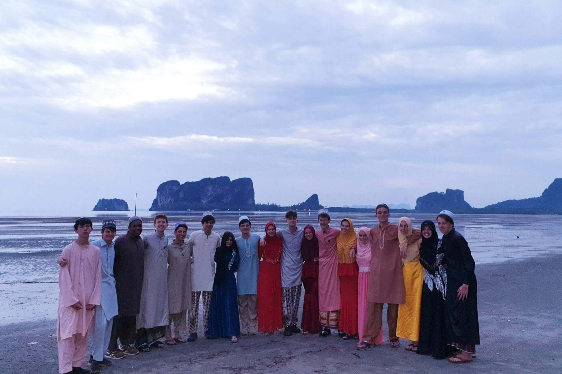 Group of students in traditional attire enjoying a beach sunset during a summer marine conservation trip in Thailand.
