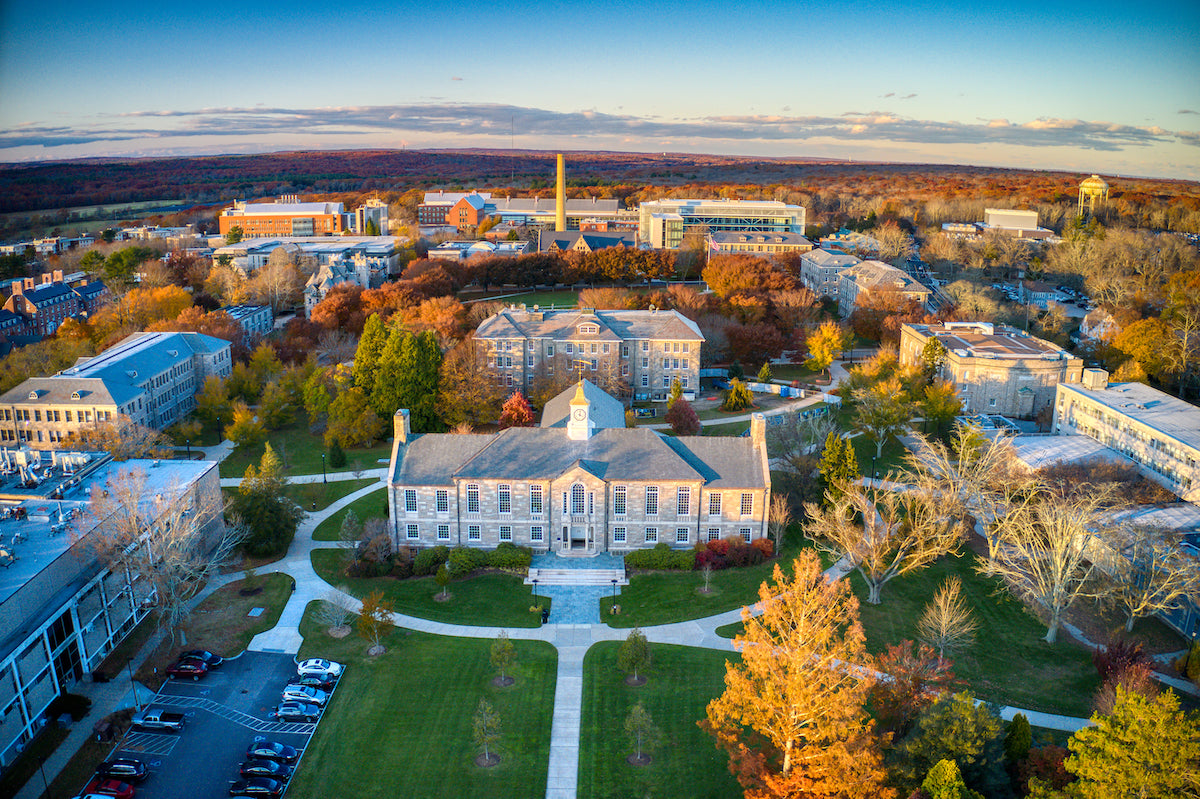 Aerial view of a college campus surrounded by colorful autumn trees, highlighting buildings and green spaces.