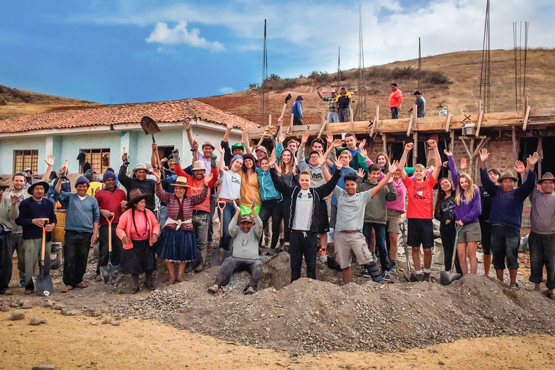 Group of diverse volunteers celebrating during a community project in a rural area, with construction in the background.
