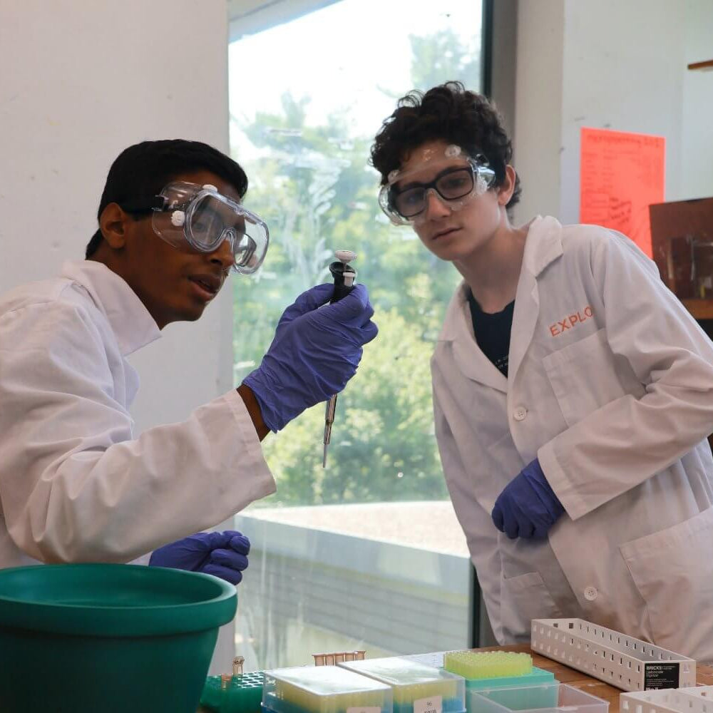 Two middle school students in lab coats engaging in a science experiment during a summer program at EXPLO.