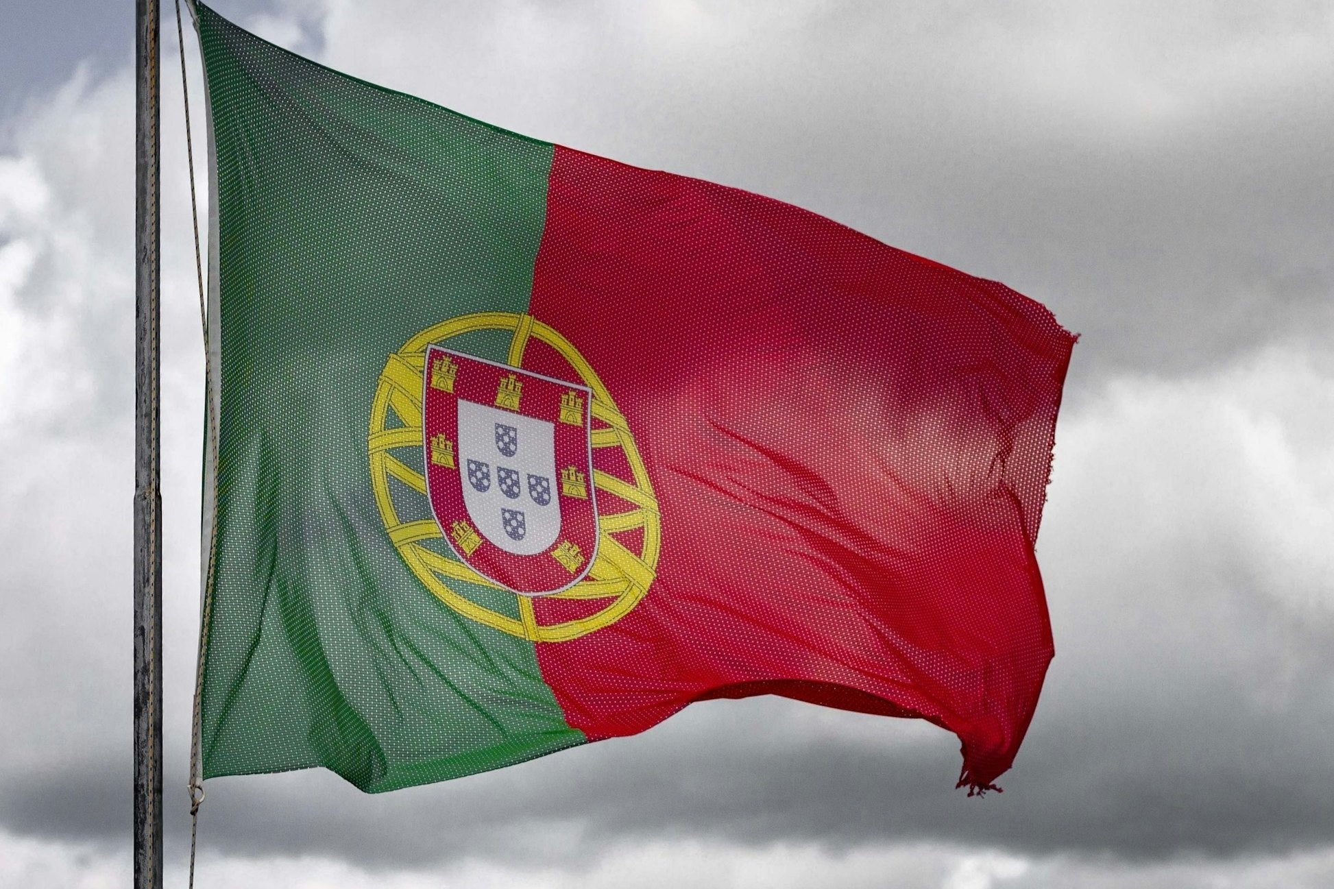 Portuguese flag waving against a cloudy sky, symbolizing culture and heritage in Lisbon.